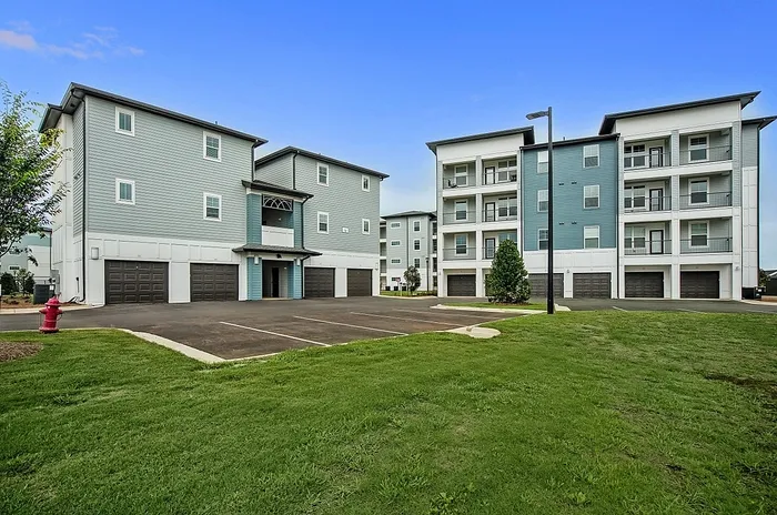 Contemporary apartment complex with spacious balconies, sleek architecture, and ample parking, set against a vibrant blue sky.