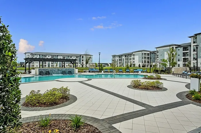 Luxurious apartment complex featuring a large, inviting pool area with lounge seating and lush landscaping.