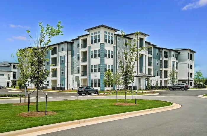 Modern apartment complex with sleek architecture, lush greenery, and ample parking, perfect for contemporary living.