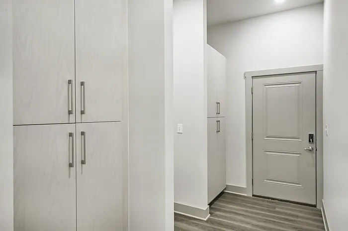Modern entryway with sleek white cabinetry and contemporary gray door, offering ample storage and a stylish welcome.