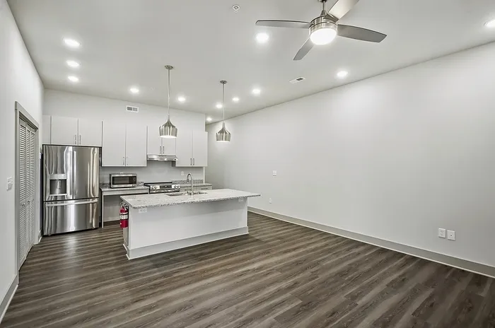 Modern kitchen with sleek stainless steel appliances, elegant lighting, and spacious granite countertops in a contemporary open-layout apartment.