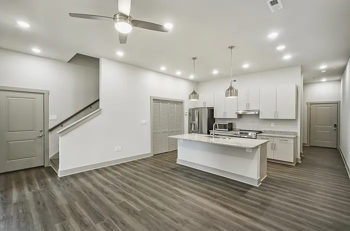 Modern open-concept kitchen with sleek white cabinetry, stylish pendant lighting, and spacious island in a bright apartment.