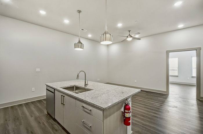 Modern open-concept kitchen with sleek granite countertops, stylish pendant lights, and rich wooden flooring, leading into a spacious living area.