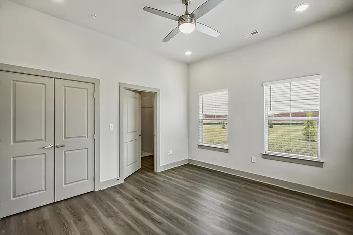 Bright and spacious bedroom featuring elegant hardwood floors, modern ceiling fan, and large windows with tranquil outdoor views.