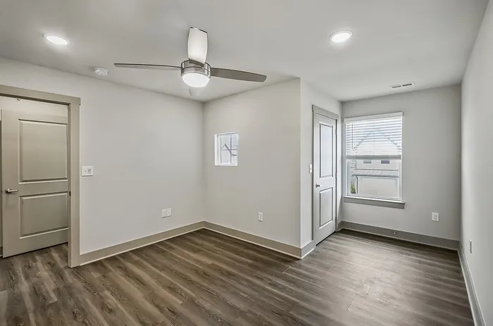 Bright minimalist room with sleek wood floors, modern ceiling fan, and ample natural light from large window.