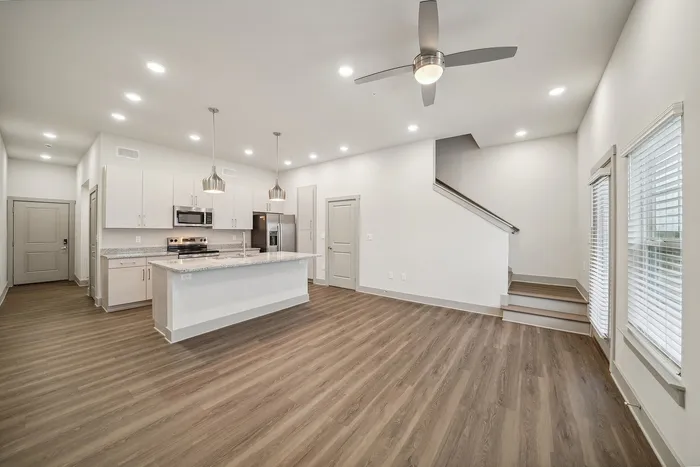 Contemporary open-plan kitchen and living area with modern fixtures, wood-look flooring, and ample natural light, featuring a sleek staircase for added style.