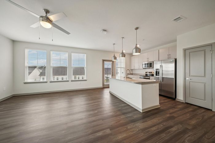 Bright open living space with sleek modern kitchen, stainless steel appliances, and elegant pendant lighting.