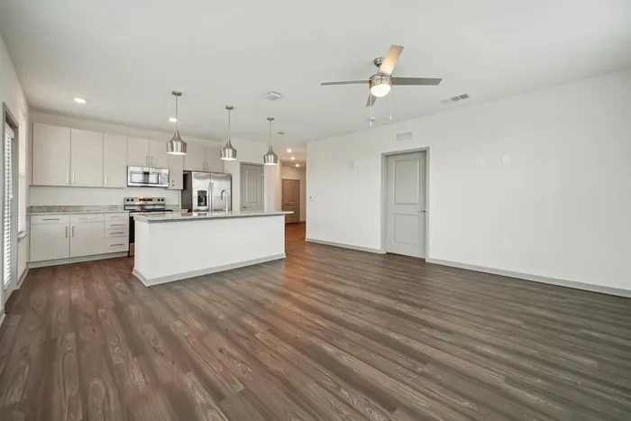 Modern open-concept kitchen with sleek stainless steel appliances, pendant lighting, and elegant wood flooring, perfect for entertaining.