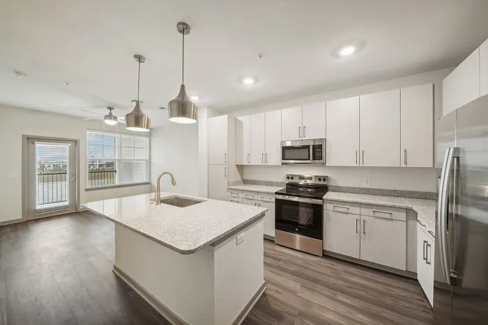 Modern kitchen featuring sleek granite countertops, stainless steel appliances, and stylish pendant lighting, seamlessly connecting to a bright living space with elegant wood flooring.