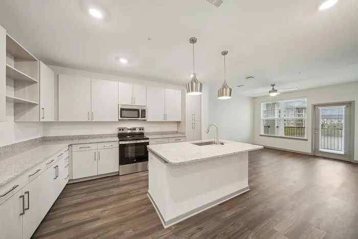 Modern open-concept kitchen with sleek cabinetry, granite countertops, stainless steel appliances, and elegant pendant lighting overlooking a bright living area with hardwood floors.
