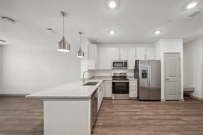 Sleek modern kitchen with stainless steel appliances, elegant pendant lighting, and a spacious granite countertop in a pristine open-plan layout.