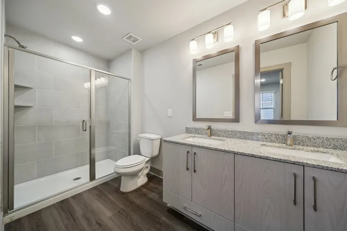 Modern bathroom with elegant double vanity, granite countertops, and spacious walk-in shower, featuring sleek tile work and contemporary lighting.