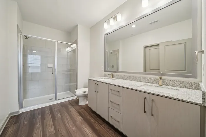 Modern bathroom boasting sleek dual-sink vanity, elegant granite countertops, and a spacious glass-enclosed shower.