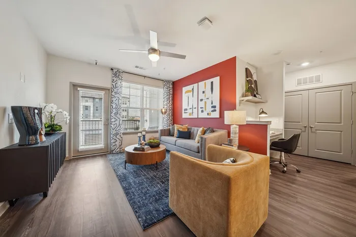 Modern living room with chic decor, featuring a cozy gray sofa, vibrant orange accent wall, and stylish lighting, complemented by large windows and elegant furnishings.