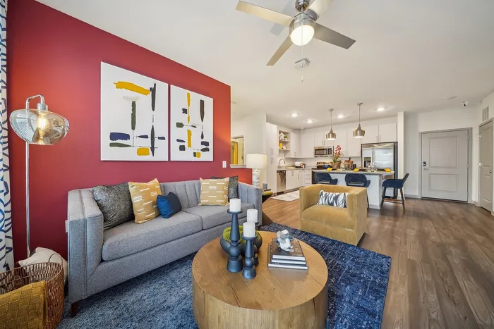 Modern open-concept living room with vibrant red accent wall, stylish gray and mustard seating, and sleek kitchen in the background.