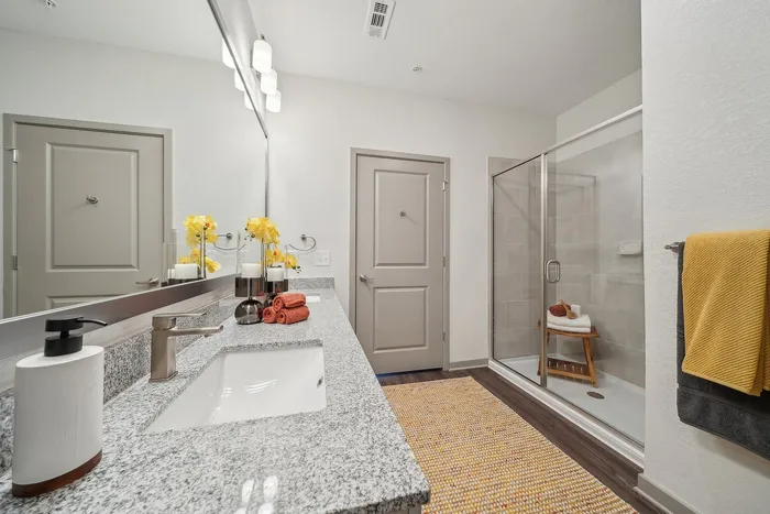 Elegant bathroom with granite countertop, double sinks, and contemporary glass shower. Bright yellow accents add a touch of warmth.