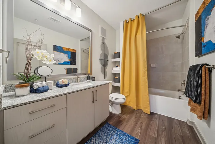 Sleek modern bathroom with elegant granite countertop, vibrant yellow shower curtain, and chic artwork enhancing a luxurious feel.