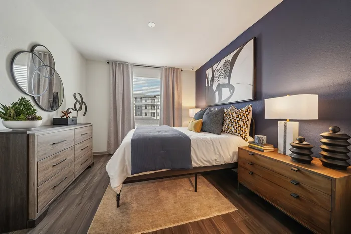 Elegant bedroom with modern decor, featuring a plush bed, stylish wooden dressers, decorative mirrors, and warm ambient lighting.