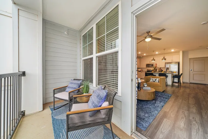 Charming apartment view showcasing a cozy balcony with stylish seating, flowing into a modern open-concept living area and kitchen with elegant lighting.