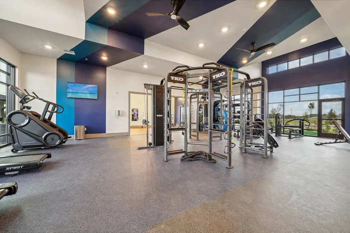 Modern fitness center with advanced exercise equipment, natural light streaming through large windows, and vibrant decor for an inspiring workout environment.