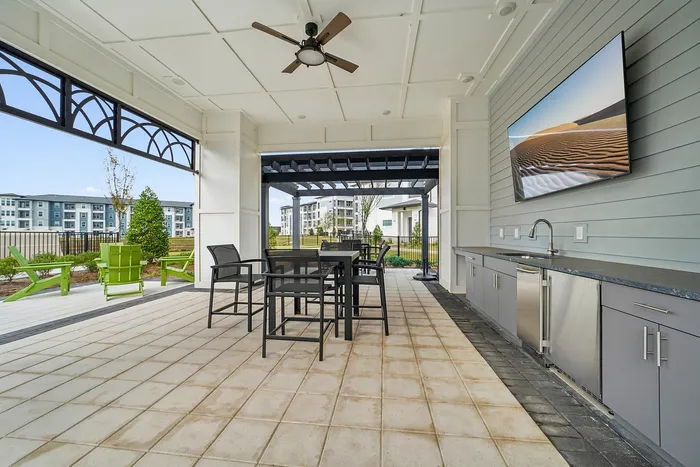 Modern outdoor entertainment area with sleek countertops, bar seating, and a ceiling fan; perfect for gatherings with scenic apartment views.