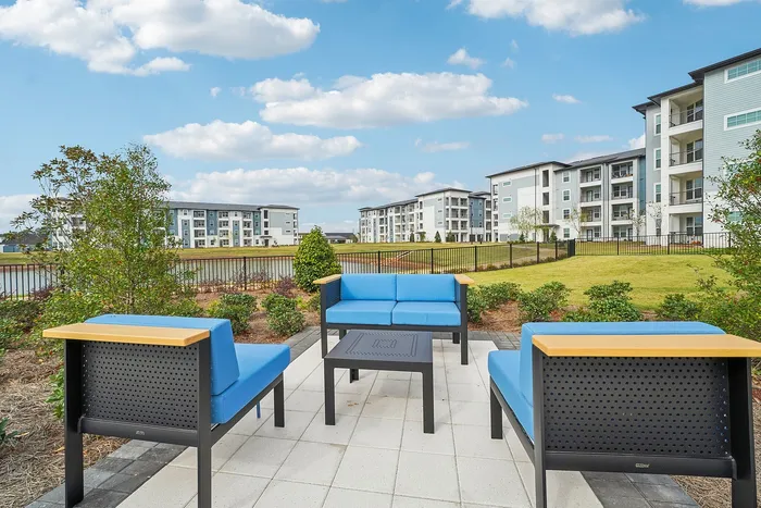 Inviting outdoor seating area with blue cushioned patio furniture, overlooking well-maintained landscapes and modern apartment buildings under a clear blue sky.