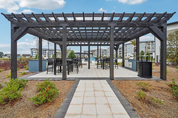 Charming outdoor patio with a modern pergola, offering elegant seating and lush garden surroundings, perfect for relaxation.