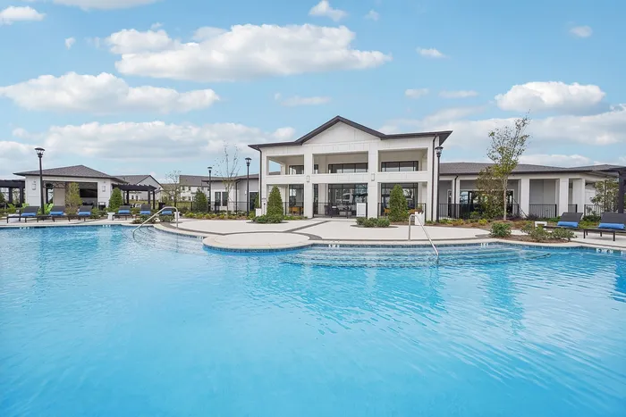Luxurious apartment complex featuring a sparkling swimming pool with modern lounge chairs under a bright, blue sky.