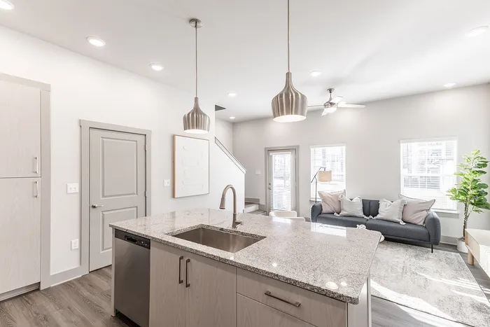 Bright modern kitchen with sleek granite countertops, pendant lighting, and open living area featuring cozy seating and abundant natural light.