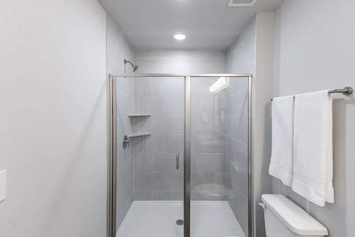 Modern bathroom featuring a sleek glass shower with gray tile walls and cozy white towels, exuding contemporary elegance.