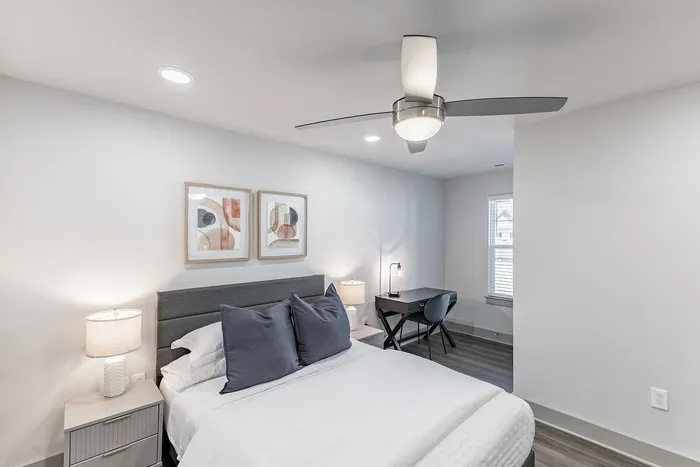 Contemporary bedroom with stylish decor, featuring a cozy bed, elegant artwork, and a minimalist desk setup beside a large window.