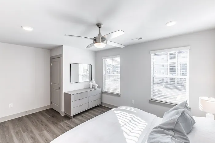 Bright and modern bedroom featuring sleek gray furniture, sunlit windows, and a stylish ceiling fan.