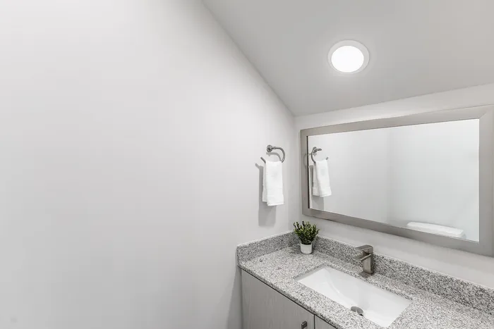 Sleek and contemporary bathroom featuring a stylish granite countertop, large mirror, and modern fixtures for a luxurious touch.