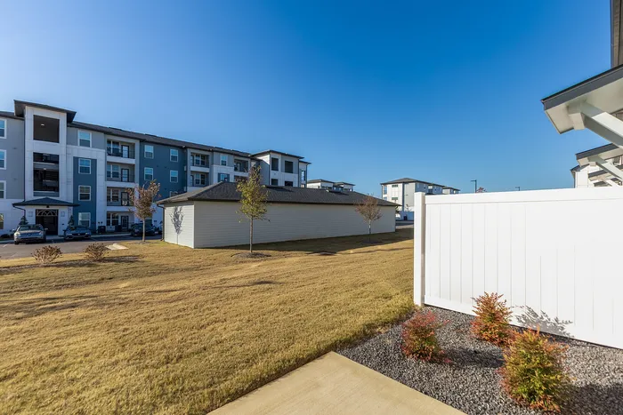 Modern apartment complex under a clear blue sky, featuring well-maintained landscaping and ample parking.