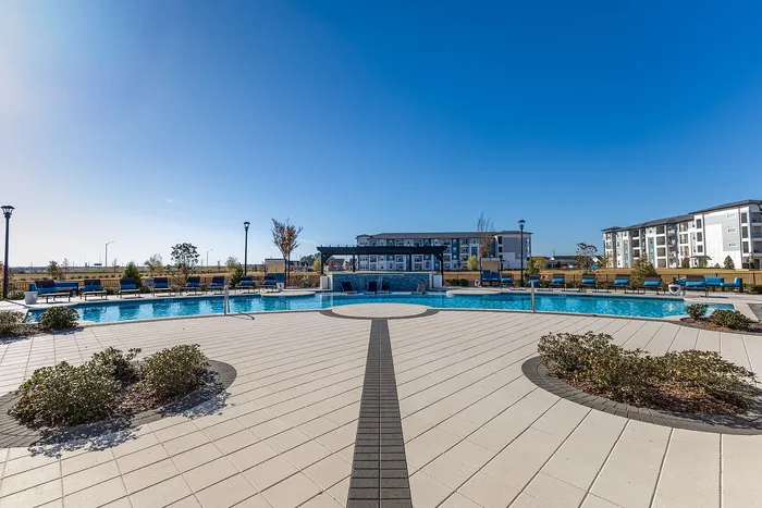 Luxurious apartment complex showcasing a stunning outdoor pool with ample seating, set against a clear blue sky.
