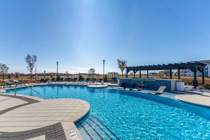 Inviting outdoor swimming pool with stylish lounge chairs and a shaded pergola area, perfect for relaxation and leisure in a vibrant community setting.