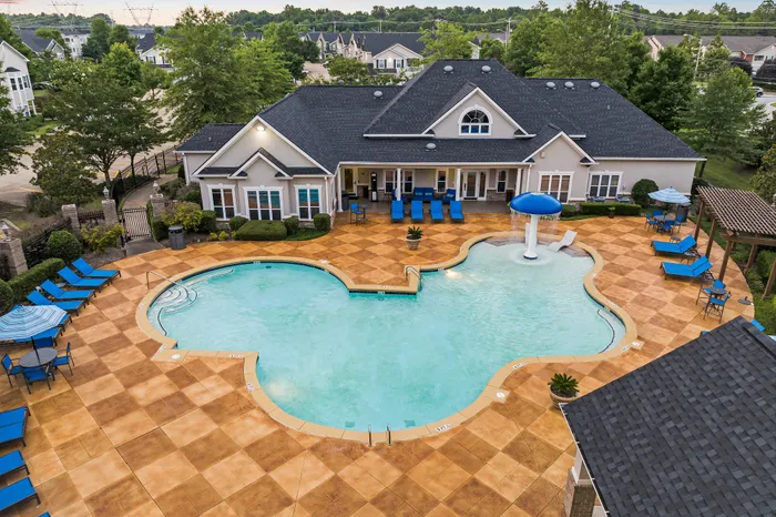 Inviting pool area with vibrant blue lounge chairs and a playful water feature, nestled next to a charming clubhouse surrounded by lush greenery, perfect for relaxation and leisure.