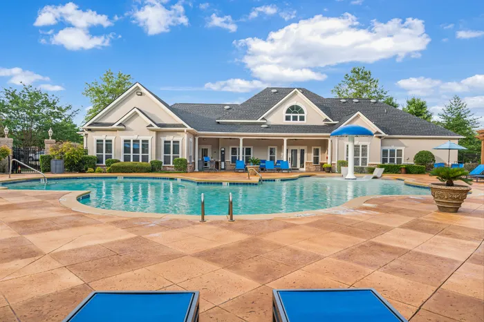 Charming apartment complex with inviting pool area, featuring elegant lounge chairs, lush landscaping, and blue sky backdrop.