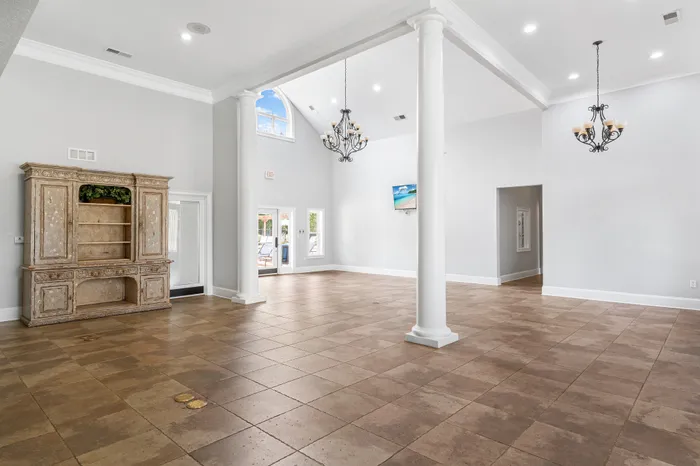 Elegant open-concept living area with high ceilings, large windows, and classical columns. Features stylish chandeliers and a vintage cabinet for added charm.