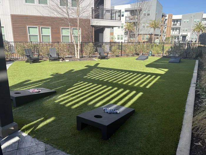 Inviting outdoor communal space featuring lush green artificial turf, modern seating, and corn hole games, surrounded by stylish apartment buildings.