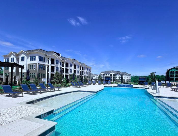 Luxurious apartment complex with a pristine swimming pool and modern architecture under a clear blue sky.