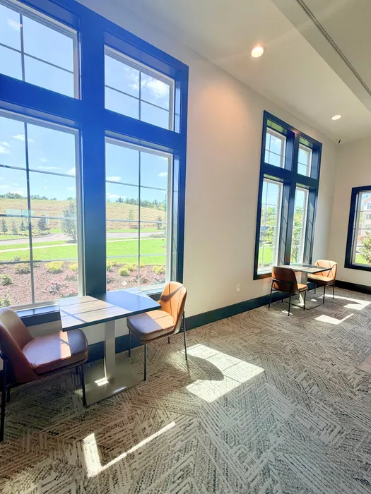 Bright social lounge with large windows, modern seating, and views of lush greenery, perfect for work or relaxation.