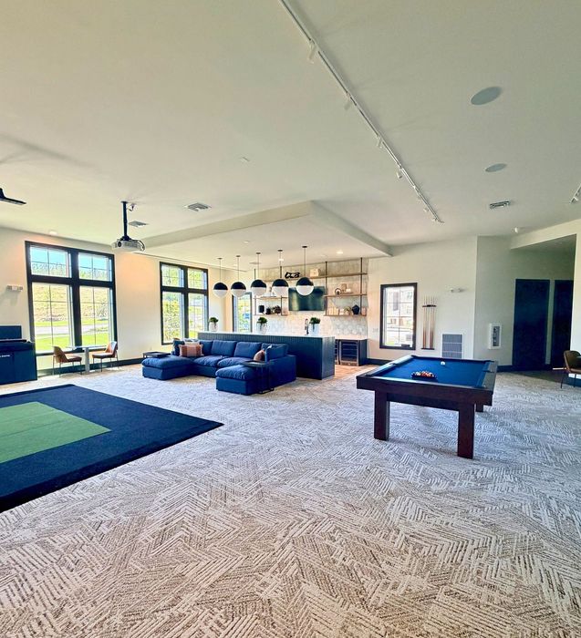 Luxurious open-concept living area with a stylish kitchen, plush sectional sofa, billiards table, and expansive windows offering natural light.