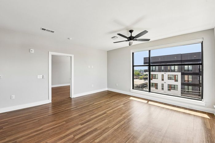 Bright modern living space with large window view, featuring elegant wood floors and sleek ceiling fan.