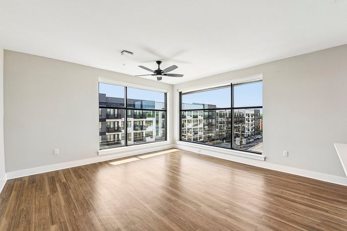Bright, modern apartment with floor-to-ceiling windows and stunning city views, featuring elegant hardwood floors and a sleek ceiling fan.