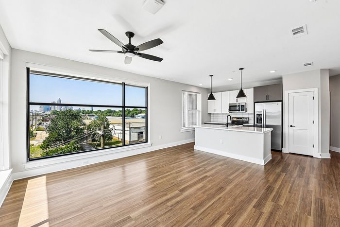 Bright and modern open-concept living space with large windows, hardwood floors, and a sleek kitchen overlooking a scenic city view.