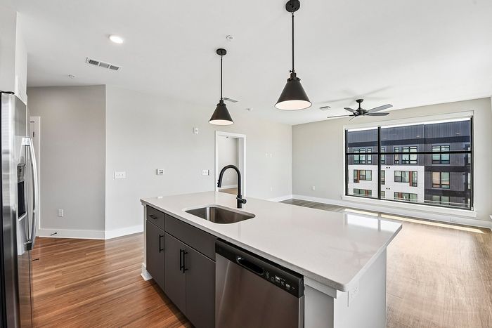 Modern apartment interior with sleek kitchen island, pendant lighting, and large window offering city views.