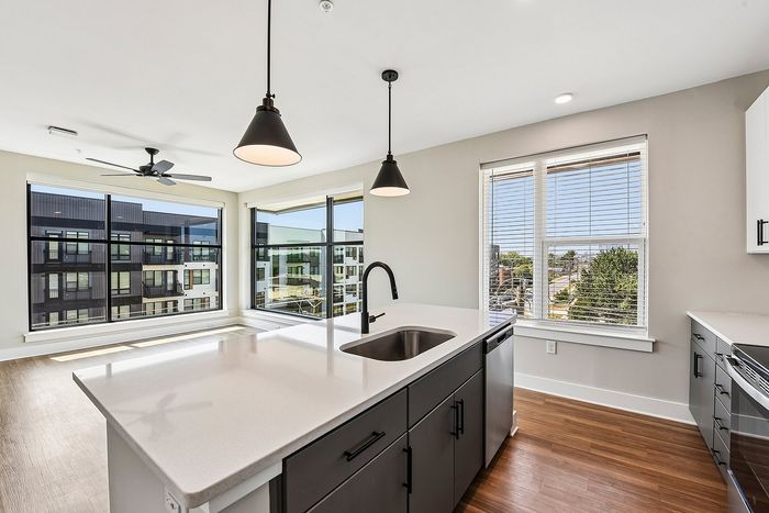 Modern kitchen with sleek white countertops, stainless steel appliances, and large windows offering stunning city and tree views.