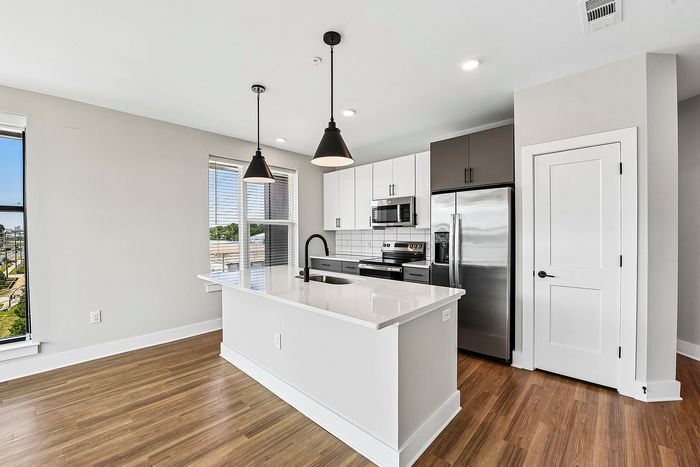 Modern kitchen with sleek design features, including stainless steel appliances, a bright white island, and elegant pendant lighting.