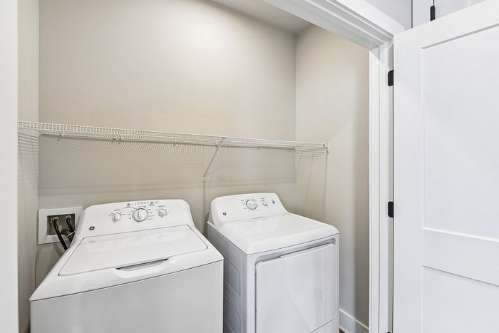 Bright utility closet featuring modern washer and dryer with convenient shelving space.